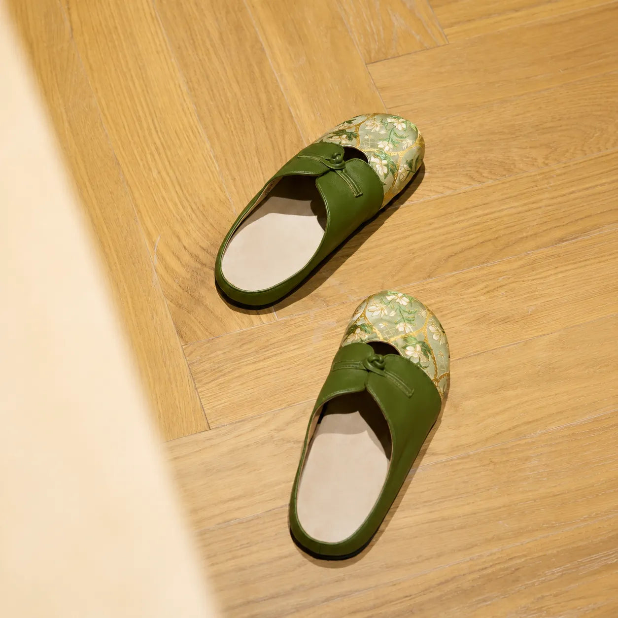 Verdant green floral brocade mules for women displayed on a warm wooden floor.