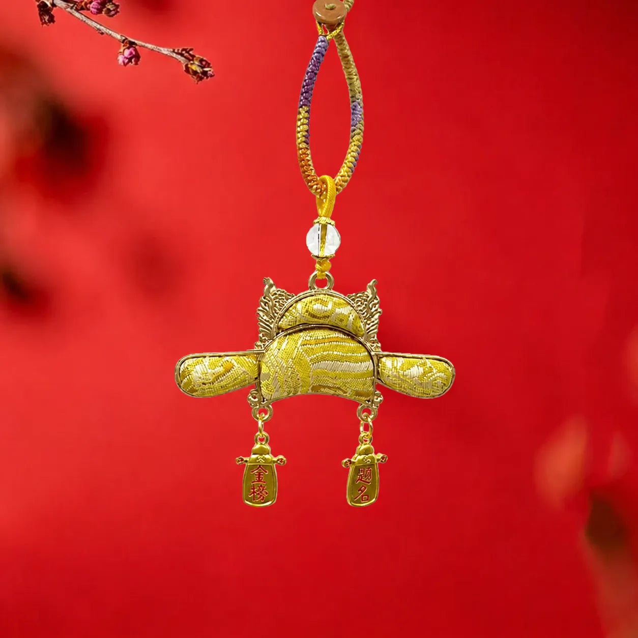 Yellow Nanjing Yunjin brocade Imperial Scholar Hat bag charm displayed against a red background with gold details and blessing pendants for exam success.