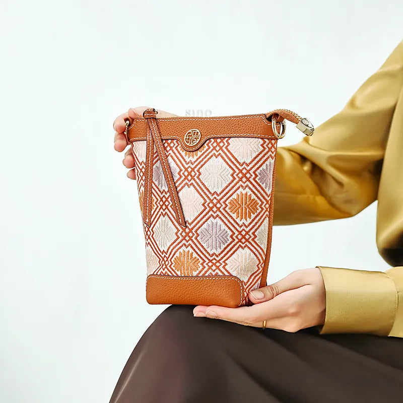 Model sitting with Zhuang brocade chrysanthemum meander motif leather bucket bag on knee.