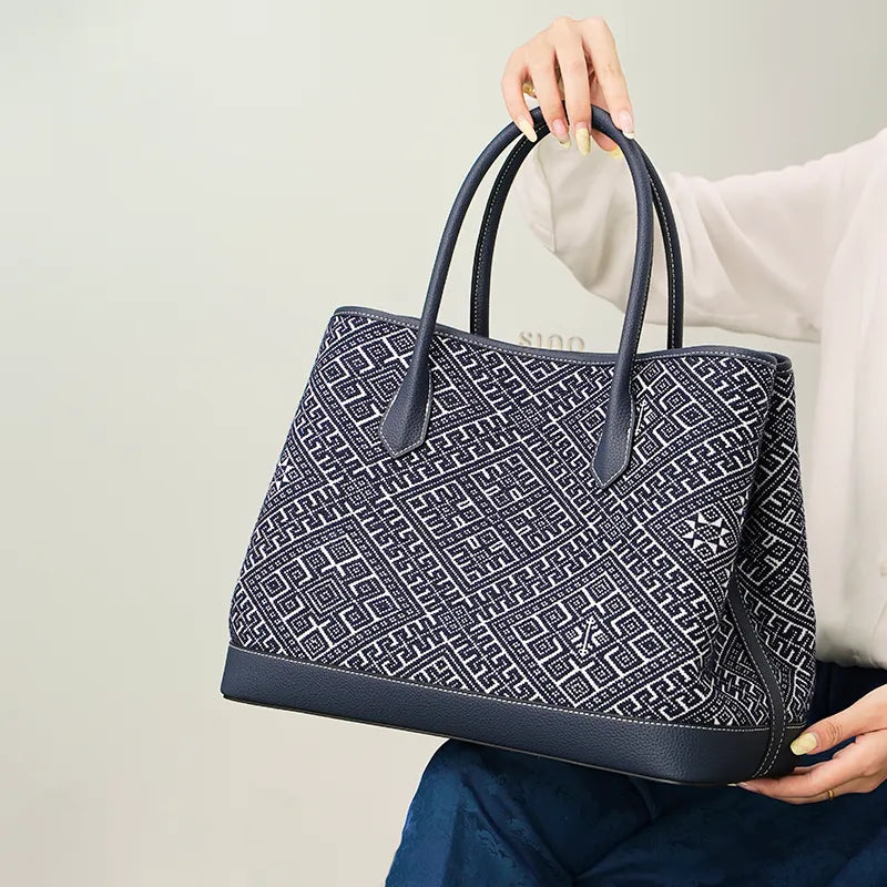 Elegant model in a blue dress sitting with the Zhuang Brocade Embroidered Leather Shoulder Bag resting on her knees, highlighting its compact yet functional size (36cm length).
