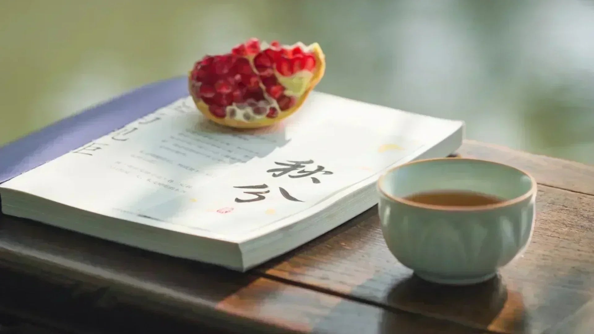 Half-opened pomegranate on a book with the Chinese character "Qiufen" (Autumn Equinox), beside a ceramic tea cup on a wooden table—capturing the serene vibe of the 24 Solar Terms.