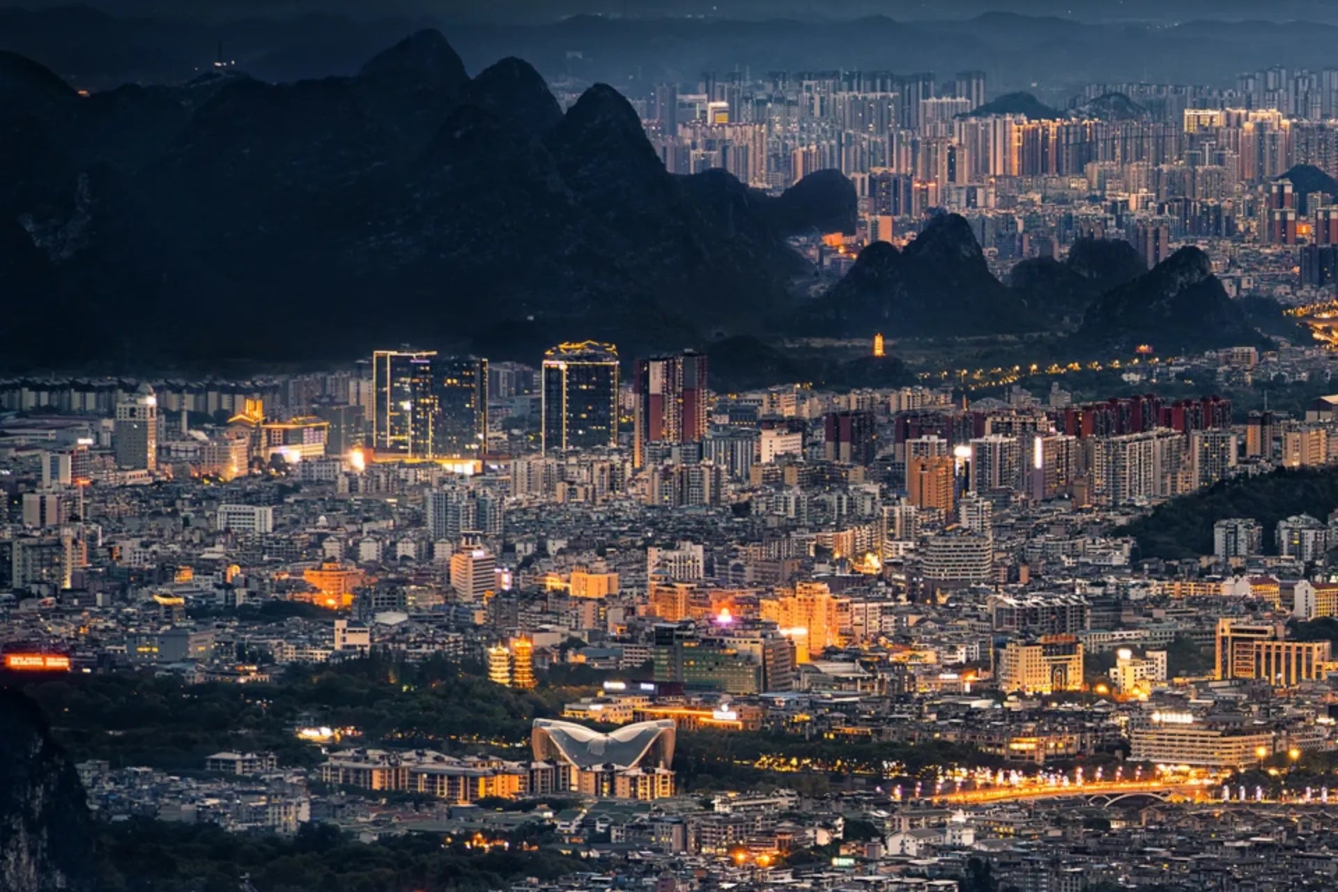 Guilin city skyline at dusk with illuminated buildings and dramatic karst mountains, featured as the cover image for a Guilin China travel guide.