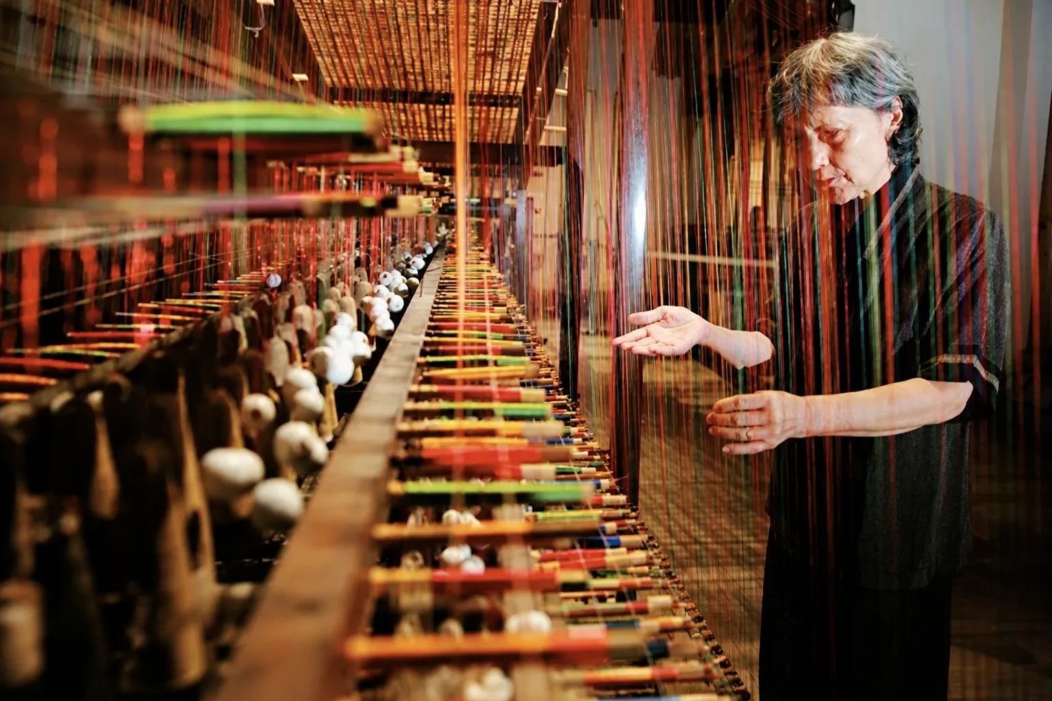 Qian Xiaoping, contemporary master of Chinese Song Brocade, examining silk threads on a traditional weaving loom.