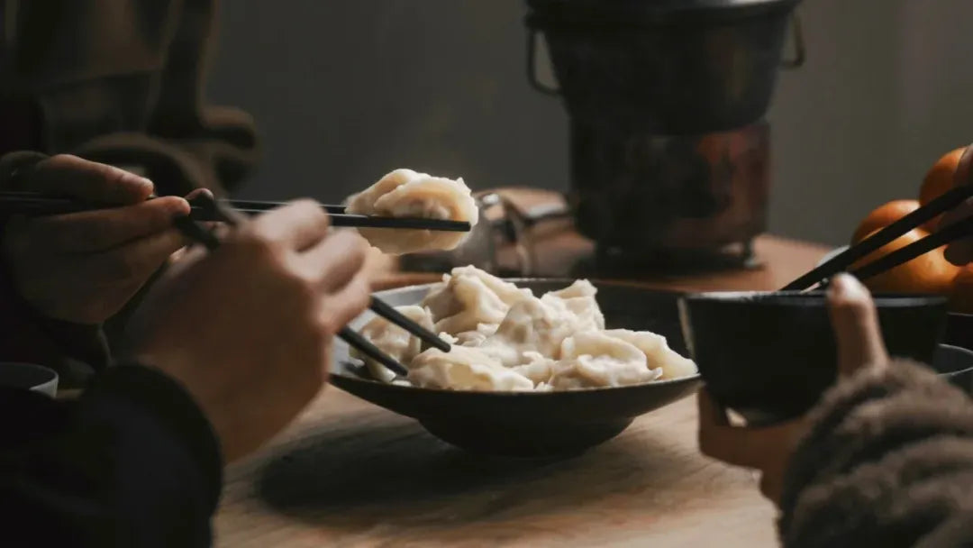 Warm Winter Solstice (Dongzhi) feast: Hands with chopsticks holding dumplings.