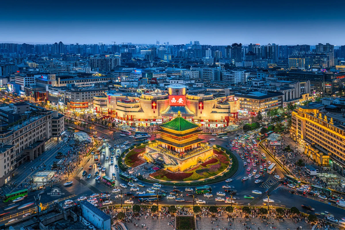 Aerial view of Xi'an Bell Tower illuminated at dusk, surrounded by busy streets and the modern skyline of China's ancient Silk Road capital.