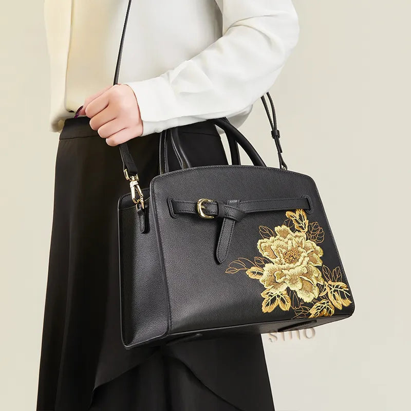 Model wearing the black peony embroidered leather top handle bag with shoulder strap.