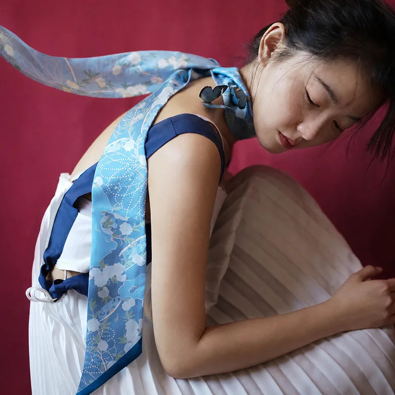 Woman styling the blue Blooming Peony Mulberry Silk Twilly around the neck, showcasing its floral print and elegant drape.