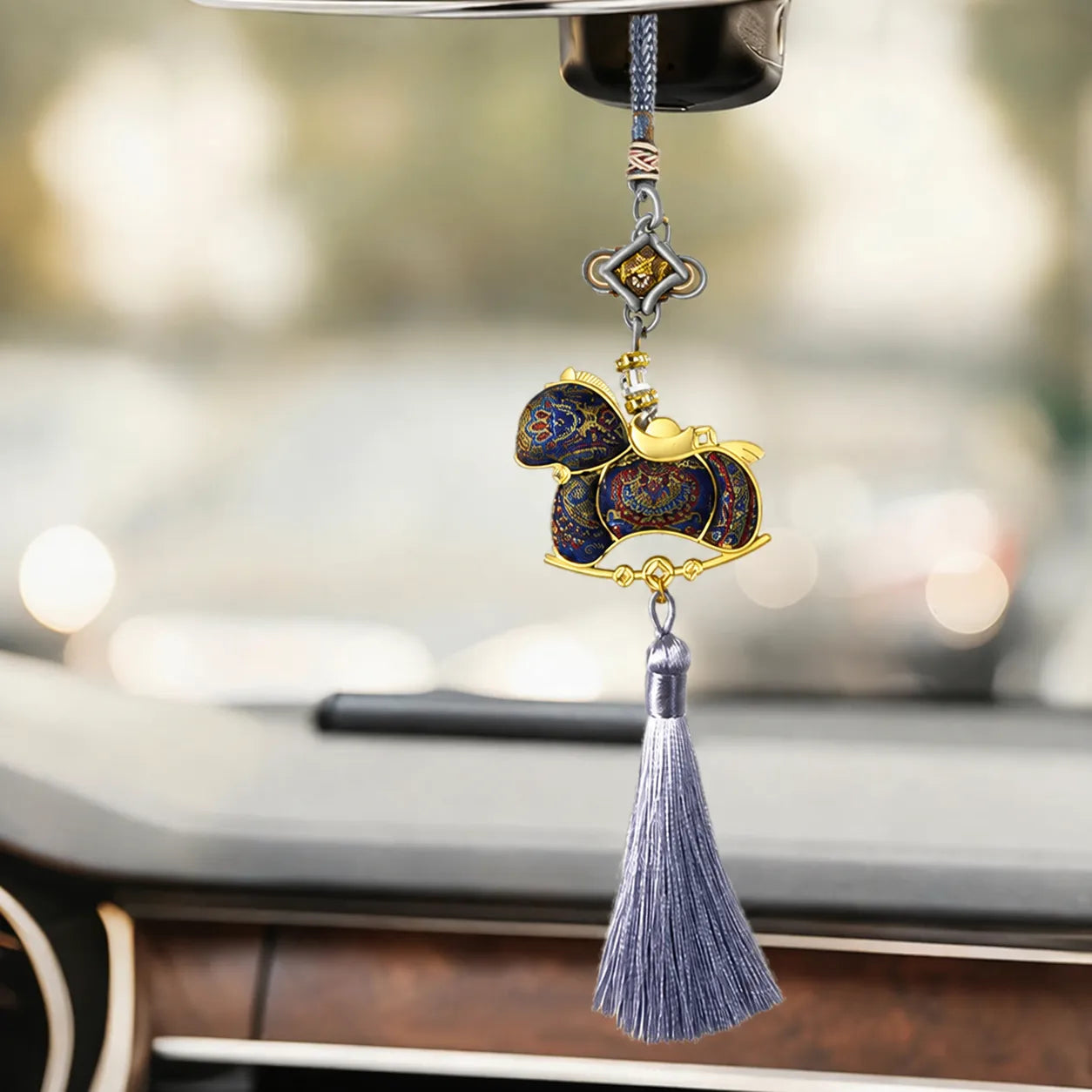 Blue Song brocade Ruyi horse tassel bag charm hanging inside a car, featuring intricate woven patterns, gold-toned edging, and a long silver-gray tassel.