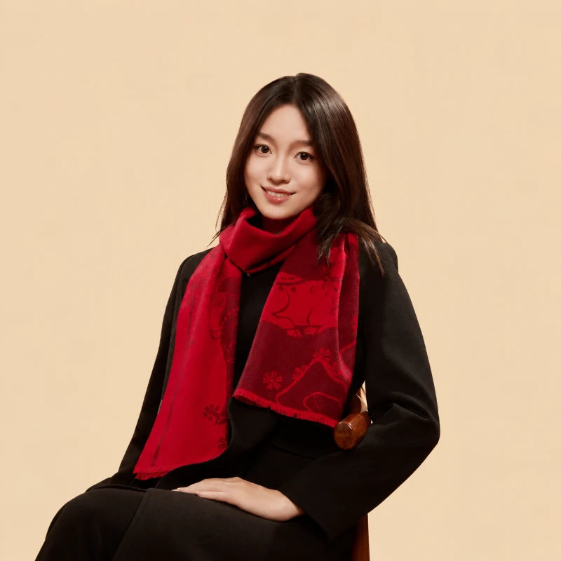Woman seated in a black outfit wearing a red cashmere-touch silk scarf wrapped loosely around her neck.