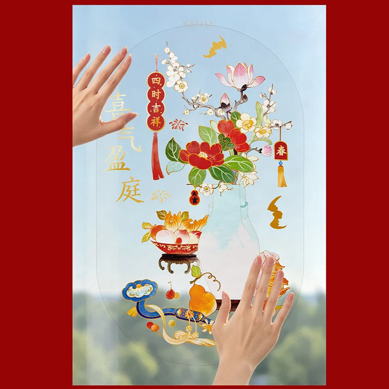 Hands applying a Chinese New Year window cling to glass, featuring a light blue vase, red and pink flowers, plum blossoms, and traditional auspicious decorations.