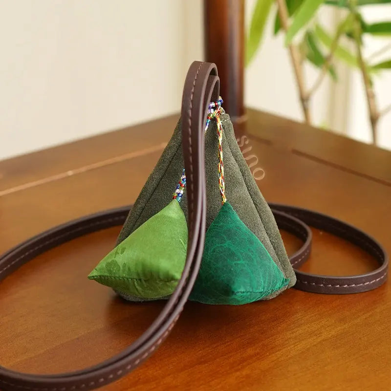 Back lifestyle view of the Chinese Xiangyunsha Silk Fortune Zongzi Coin Purse featuring green silk zongzi ornaments and a long leather strap.