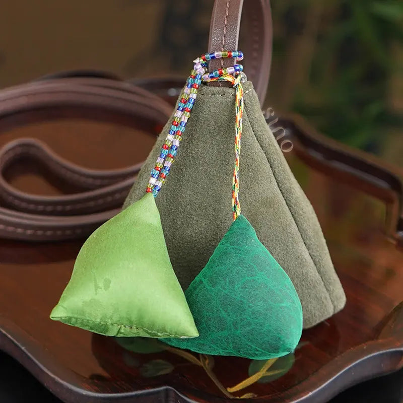 Close-up detail of the Xiangyunsha silk zongzi bag charm showing the suede texture, colorful beaded cords, green silk ornaments, and leather loop.