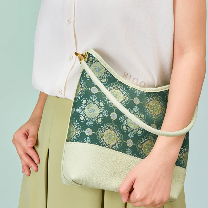 Model holding the Emerald Blossom Shu Brocade shoulder bag with ivory leather trim and an adjustable strap.