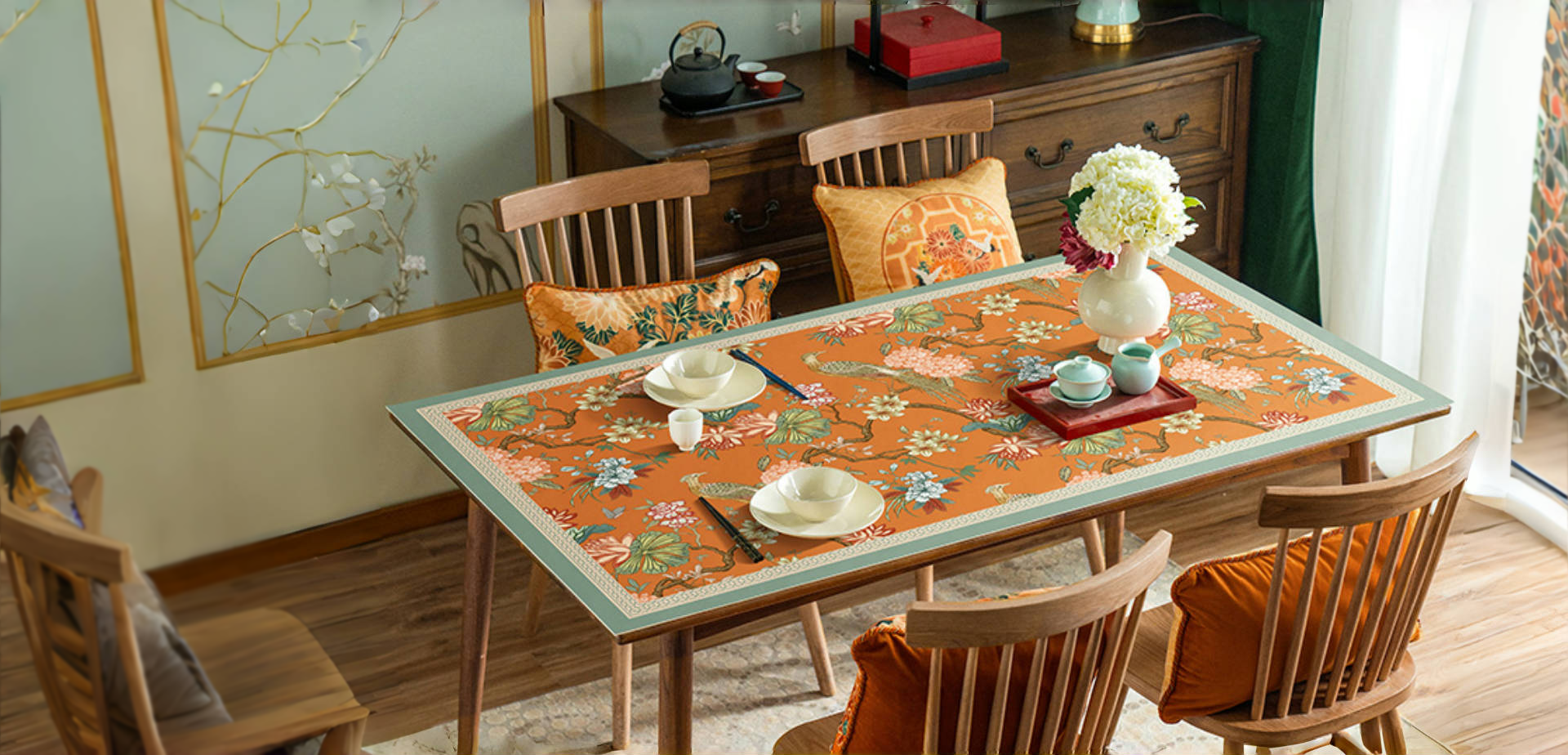 Chinoiserie floral tablecloth on wooden dining table with teaware and decorative wall art.