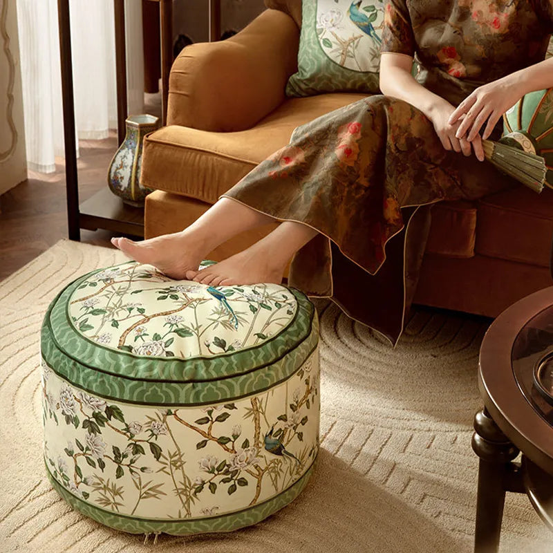 Model sitting on a sofa with both feet resting on the chinoiserie jade green couch cushion pouf.