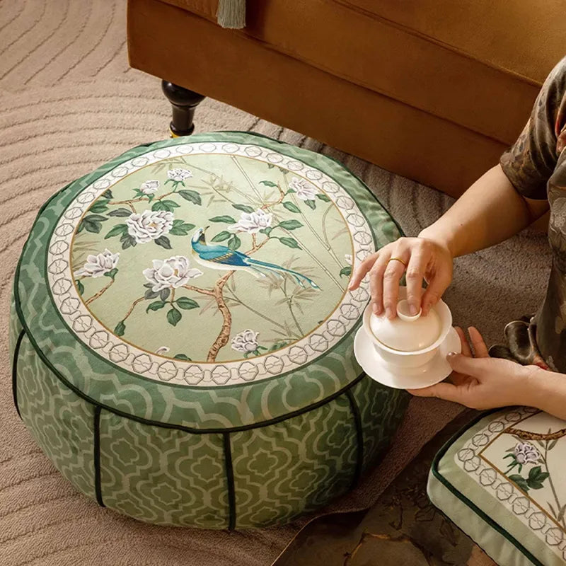 Top-down view of a model sitting beside the chinoiserie jade green floor pouf while drinking tea, showing it as living room decor.