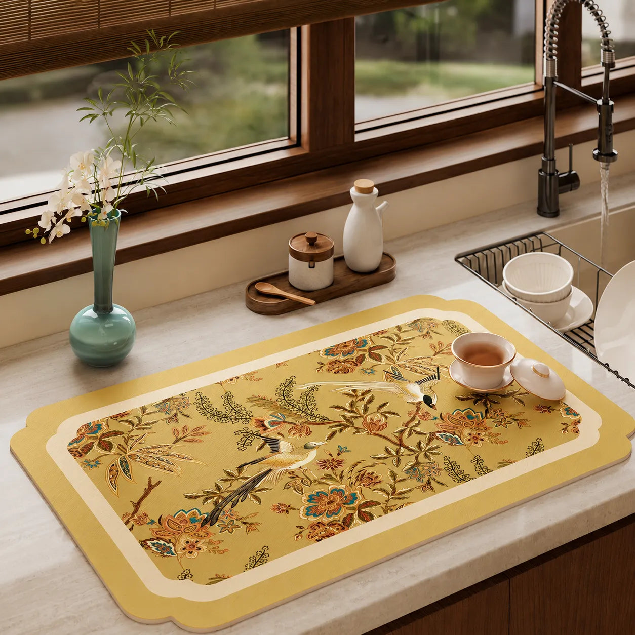 Autumn Splendor leather tea table mat with golden Chinoiserie floral and bird motifs styled with teaware on a kitchen countertop.