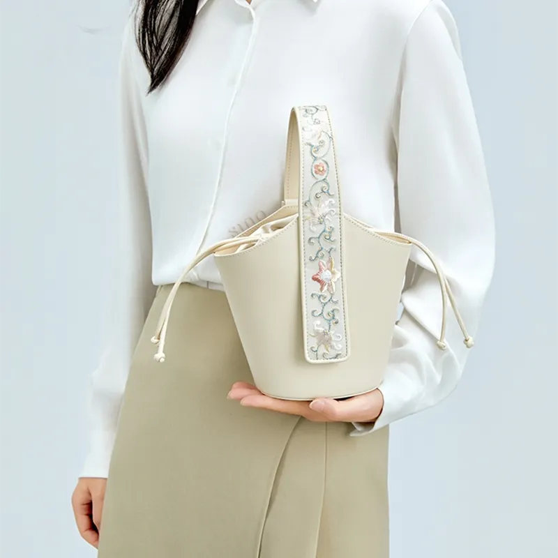 Model standing sideways holding Chinoiserie Luxury Embroidery Lotus Scroll Pattern Drawstring Bucket Bag with one hand.