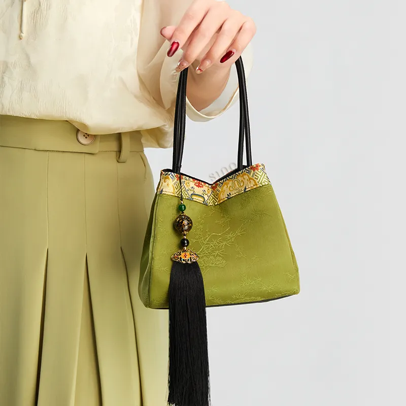 Model standing front-facing with arm raised, showing the light green bucket handbag on the arm.