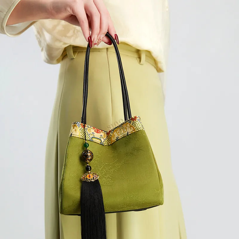 Model standing left-facing and holding the top handle, showing the front of the bucket handbag.