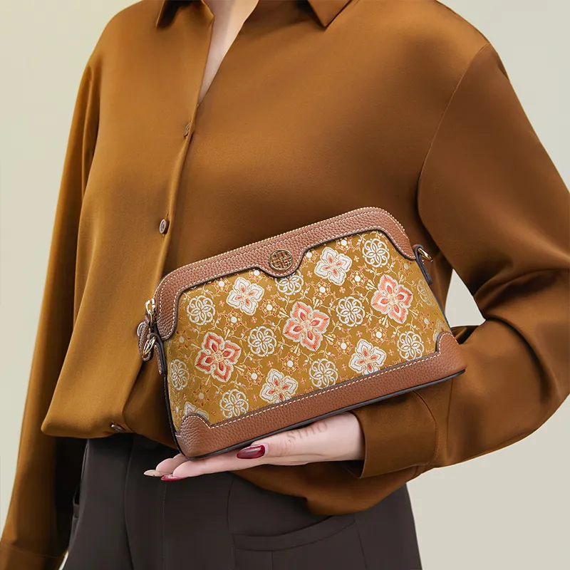 Model standing sideways holding the Persimmon Calyx Motif clutch bag with one hand angled downward.