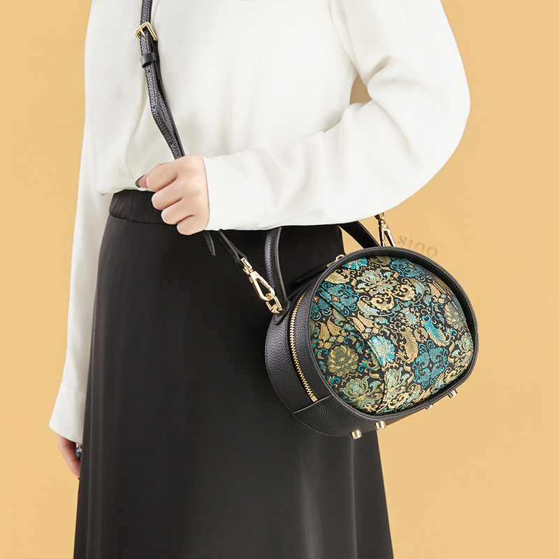 Model standing right with black Song Brocade handbag (Plantain Leaf Pattern) crossbody.