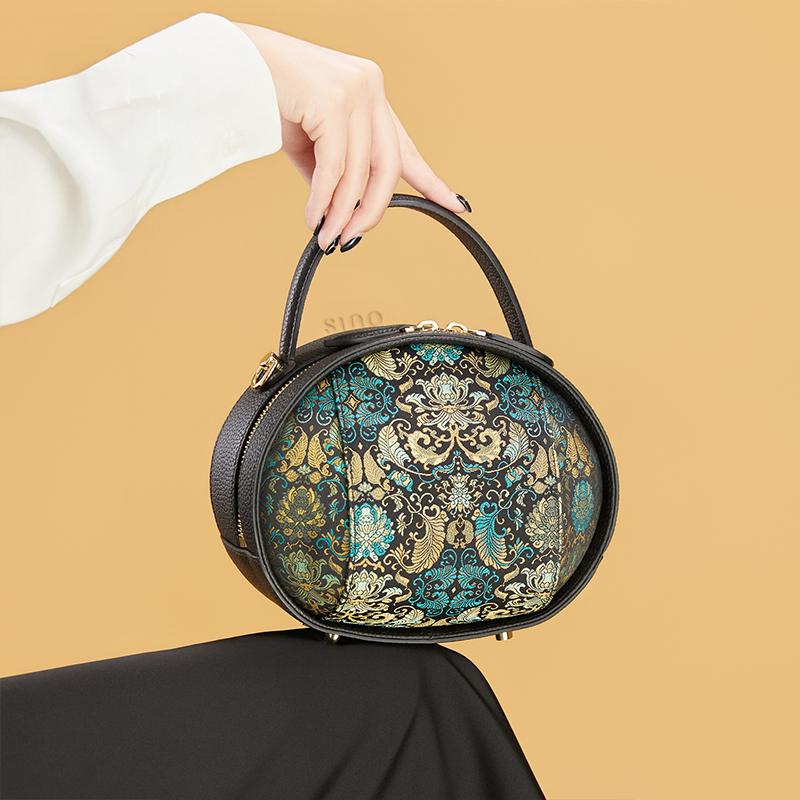 Model seated holding black Song Brocade handbag (Plantain Leaf Pattern) on knee.