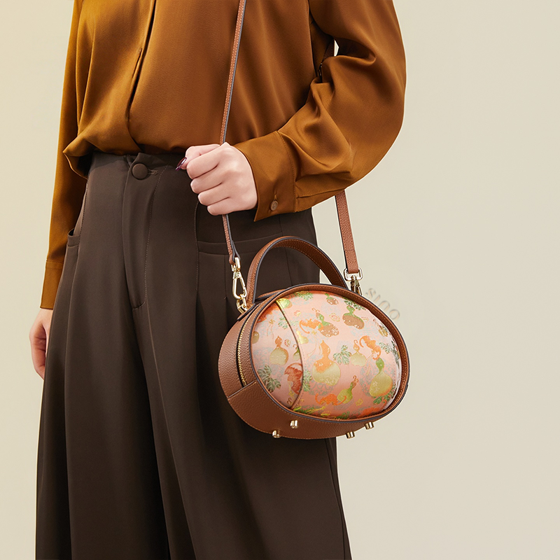 Model standing right with brown Song Brocade handbag (Gourd Pattern) over one shoulder.
