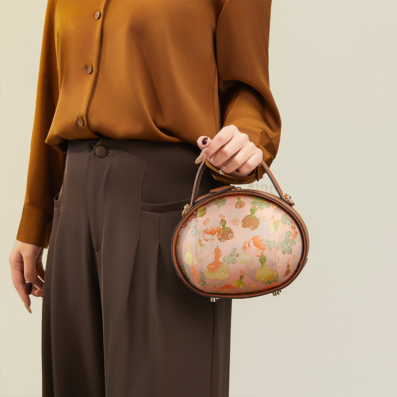 Model standing right with brown Song Brocade handbag (Gourd Pattern) as a wristlet.