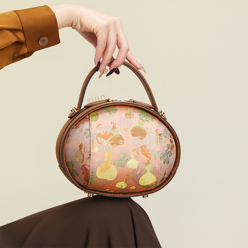 Model seated holding brown Song Brocade handbag (Gourd Pattern) on knee.