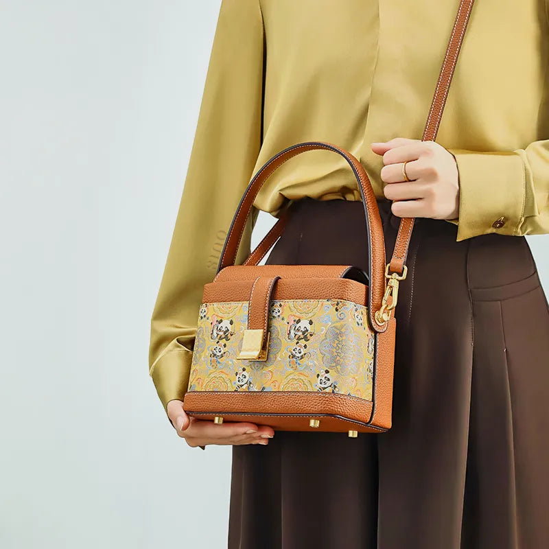 Model standing with crossbody bag at waist, supporting base with hand.