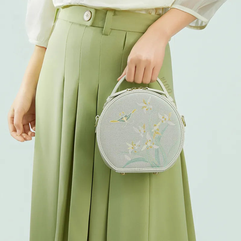 Model holding the Chinoiserie Luxury Song Brocade Phalaenopsis Orchid Round Bag in front by hand for display.