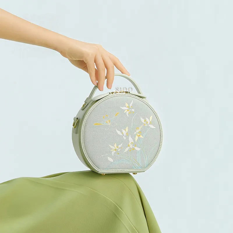 Seated model displaying the Chinoiserie Luxury Song Brocade Phalaenopsis Orchid Round Bag on the knees.