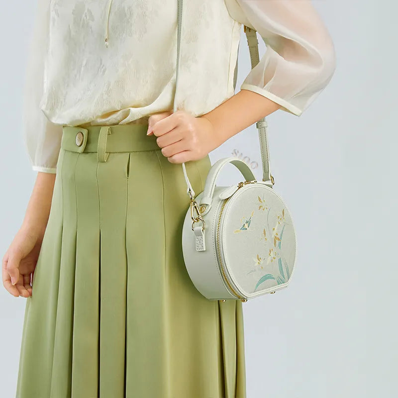 Side view of model wearing the Chinoiserie Luxury Song Brocade Phalaenopsis Orchid Round Bag as a shoulder bag, holding the strap with one hand.