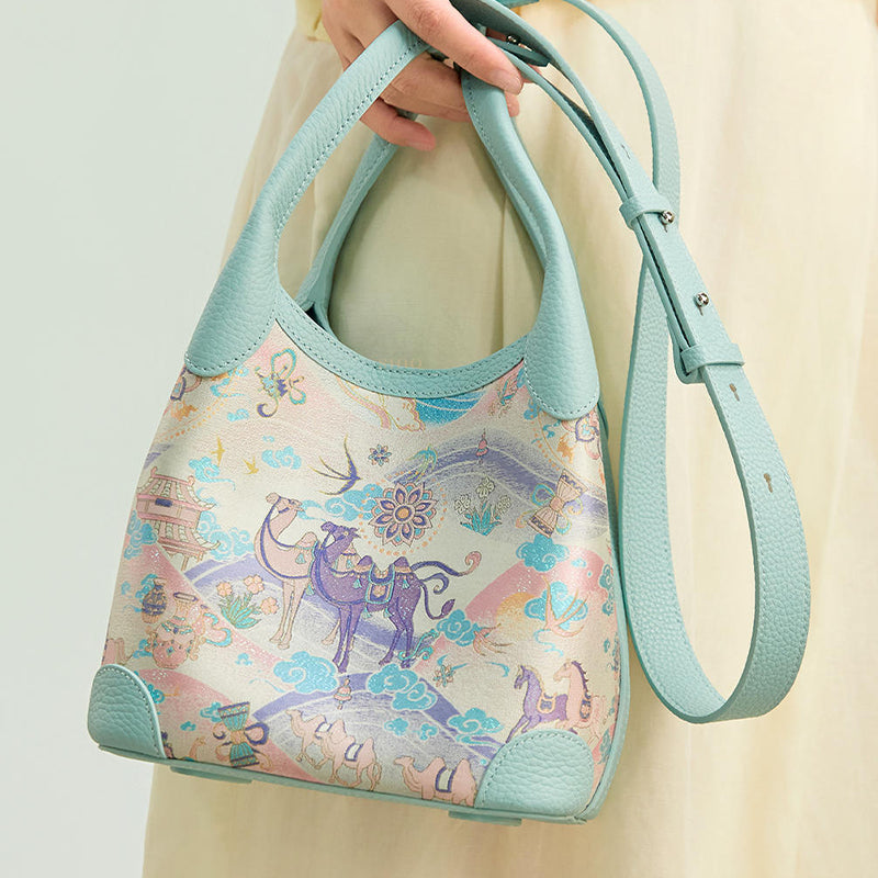Close-up model view of the Chinoiserie Song Brocade Silk Road Leather Basket Tote Bag, showing the camel and horse motif, leather handles, and long strap.