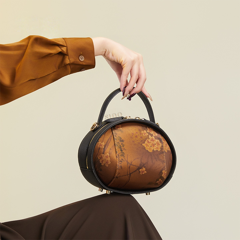 Model seated holding black Xiangyunsha handbag (Plum Blossom Print) on knee.