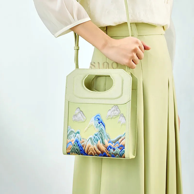 Chinoiserie Mountains Painting hand-embroidered leather bag worn with a shoulder strap, showing the structured handle and mountain embroidery.