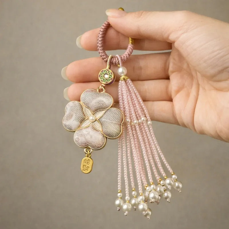 Another hand-held view of the pink Chinoiserie Song Brocade auspicious four-leaf clover tassel bag charm with pearl tassels and gold-tone accents.