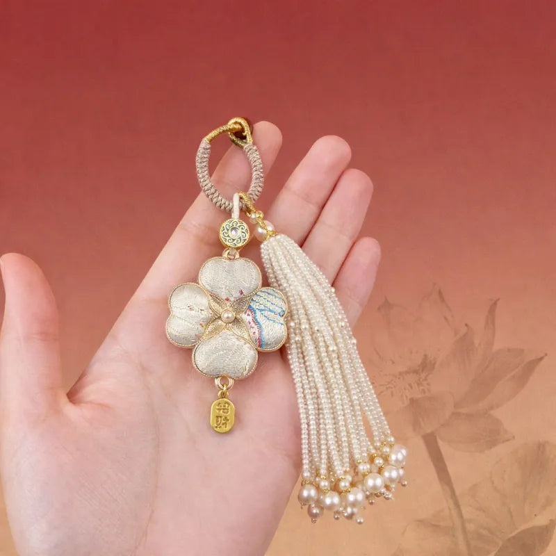 Pink Chinoiserie Song Brocade auspicious four-leaf clover tassel bag charm displayed on a hand, with pearl tassels and gold-tone trim.