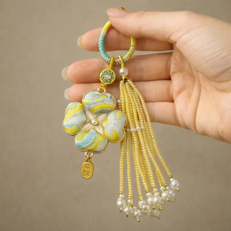 Another hand-held view of the yellow Chinoiserie Song Brocade auspicious four-leaf clover tassel bag charm with pearl tassels and gold-tone accents.