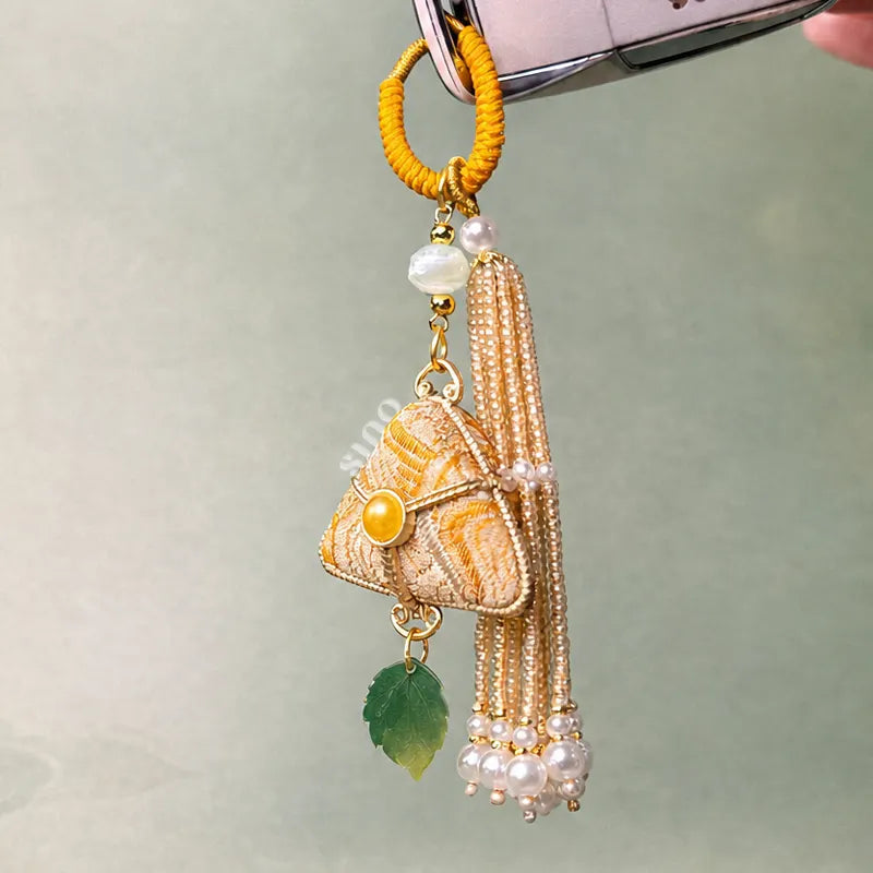 Yellow Chinoiserie Song Brocade auspicious zongzi tassel bag charm hanging from a bag, featuring pearl tassels and a green leaf pendant.