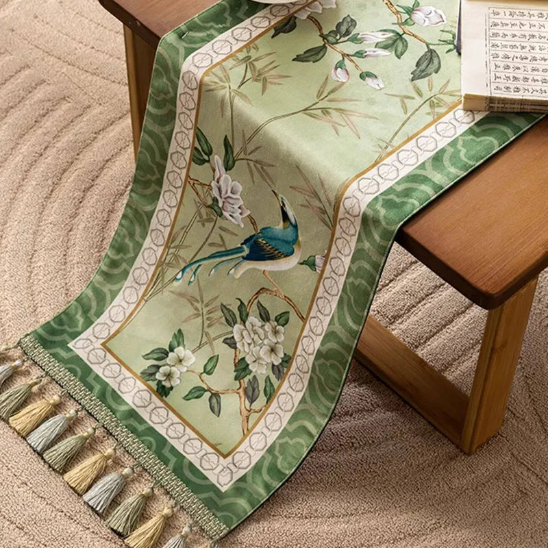 Jade green chinoiserie table runner on a table with handmade tassels hanging down from the edge.