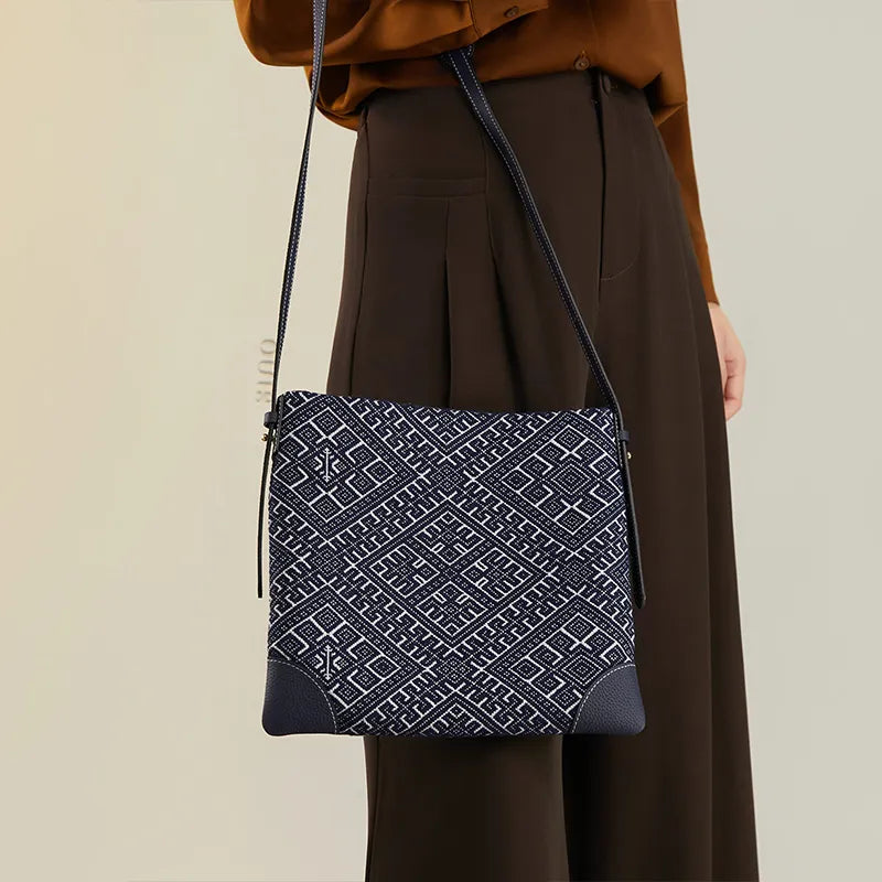 Close side view of model holding the strap of the Chinoiserie Zhuang Brocade Swallow Motif Blue Messenger Crossbody Bag, with the bag hanging naturally.