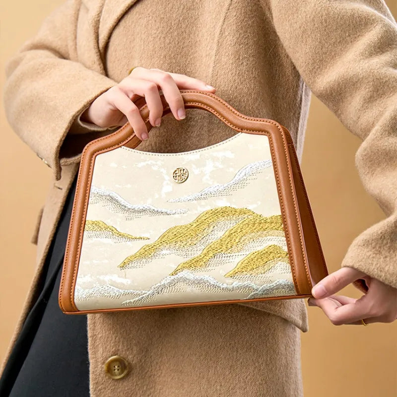 Luxury Cloud Mountain embroidery top handle bag styled with a camel coat for an elegant look.