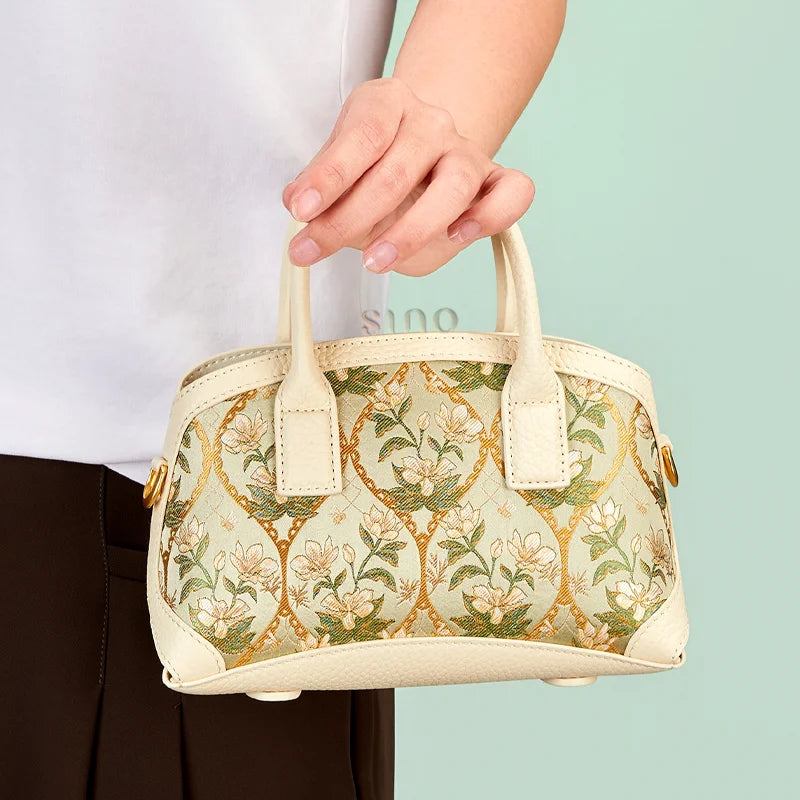 Model carrying the Verdant Floral Dayun Brocade leather top handle bag by its double handles.