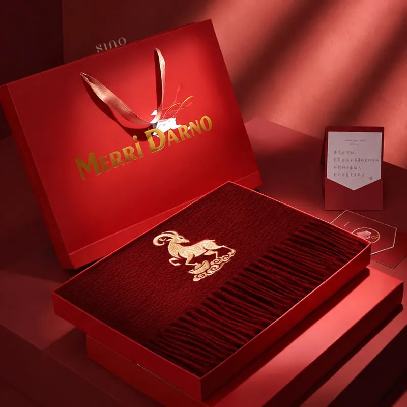 Open red gift box displaying a cashmere scarf with gold goat embroidery, matching presentation packaging, and a coordinated gift card.