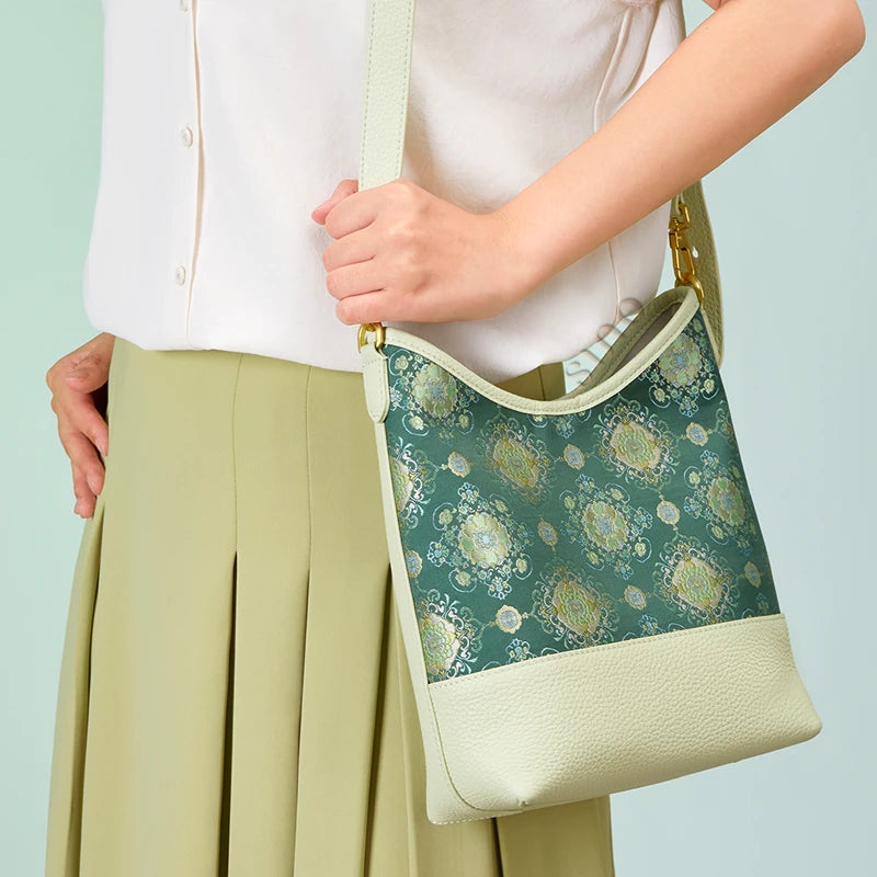 Model wearing the green Emerald Blossom Shu Brocade leather shoulder bag with a light neutral outfit.