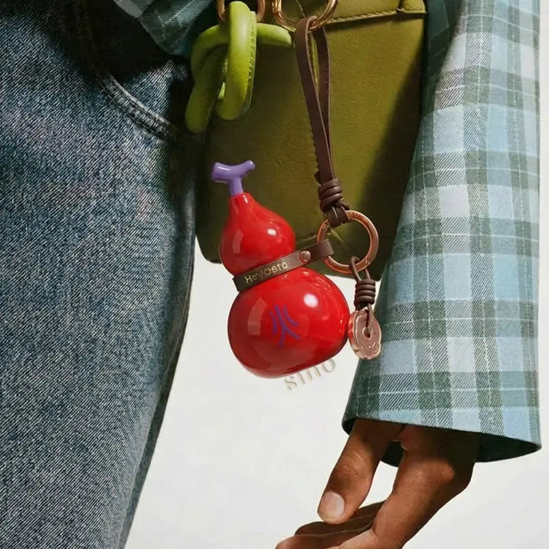 Red Fire element porcelain Hulu bag charm hanging from a bag with a brown leather strap and bronze-tone ring.