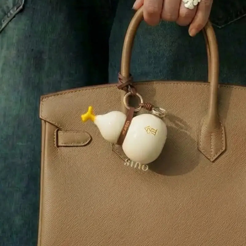 White Metal element porcelain Hulu bag charm attached to a brown handbag with a leather strap and metal ring.