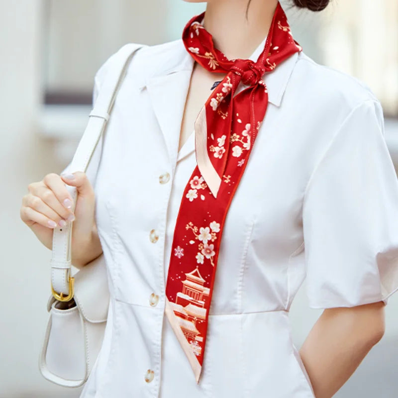 Woman wearing the red Forbidden City Snowfall & Magpie Mulberry Silk Twilly as a neck scarf with a white dress.